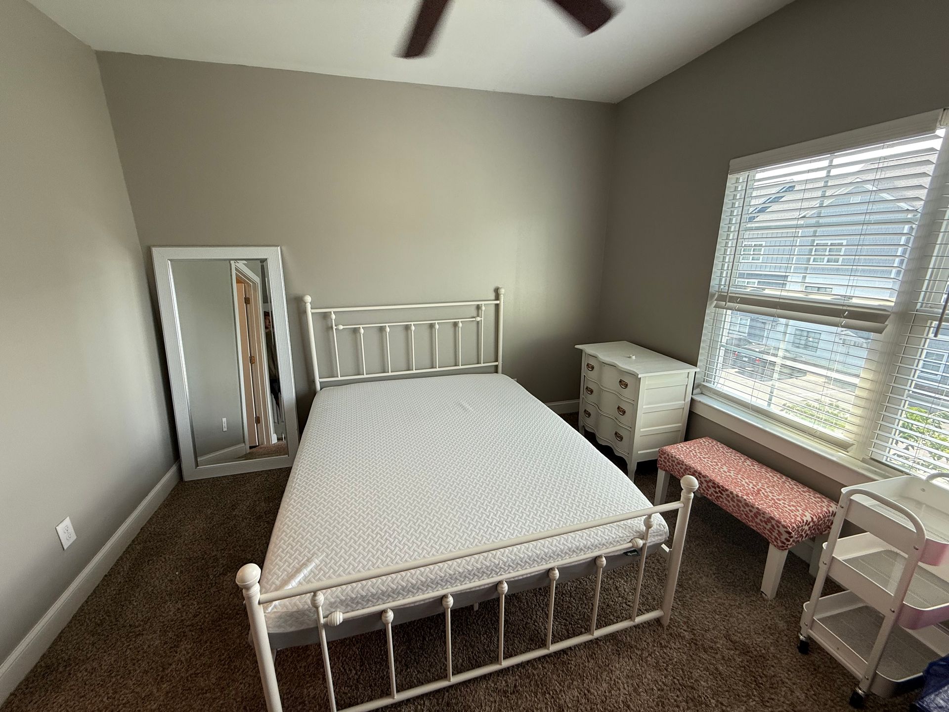 Empty bedroom with a white bed, dresser, and full-length mirror. Dark carpet and gray walls.