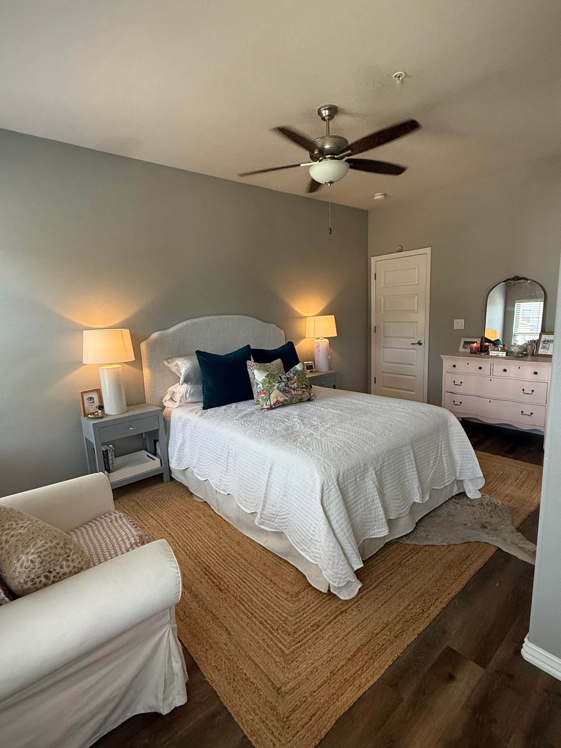 Bedroom with a bed, dresser, nightstand, and armchair; gray walls and a brown rug.