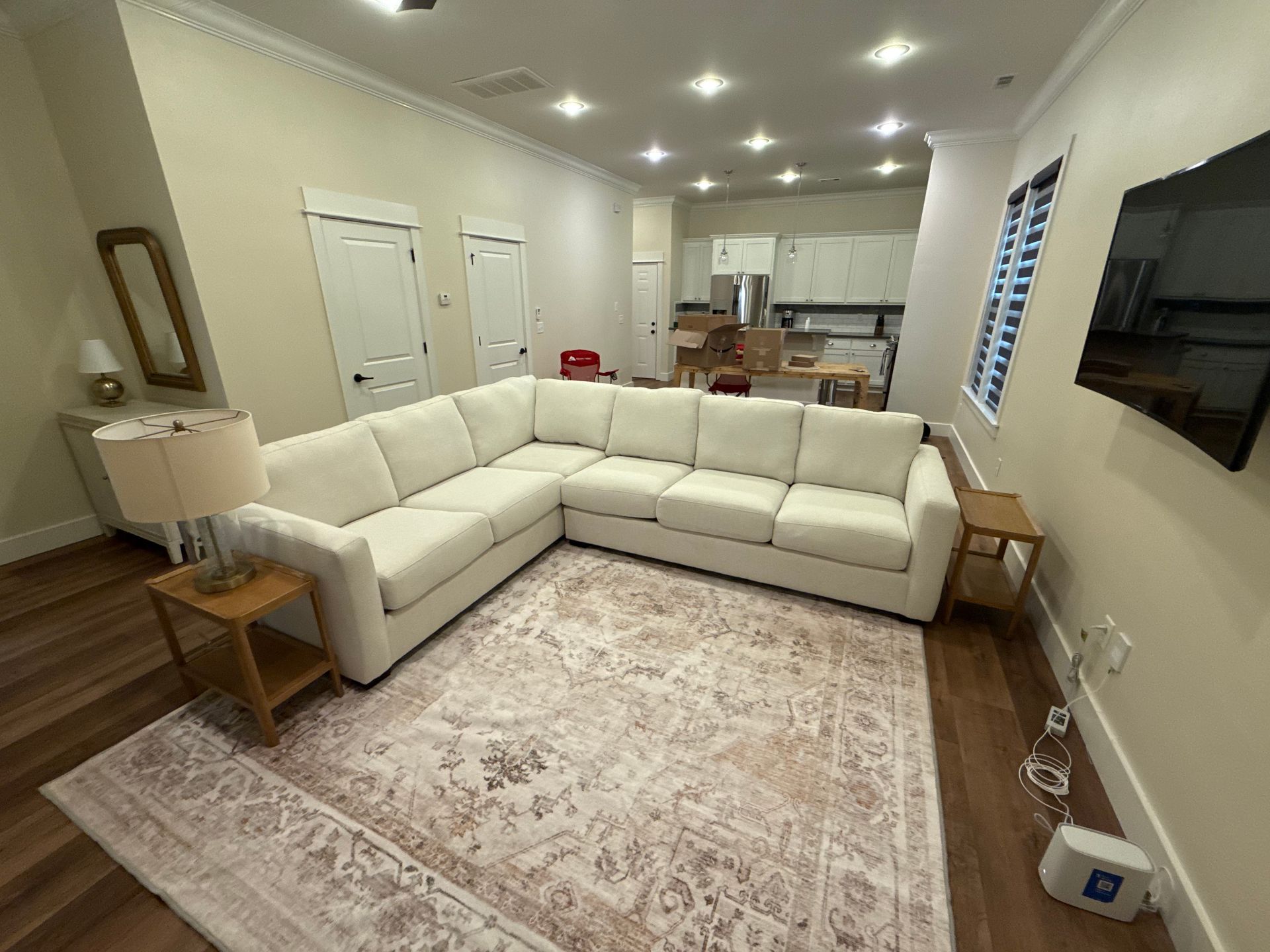 Spacious living room with a white sectional sofa, patterned rug, and open kitchen in the background.