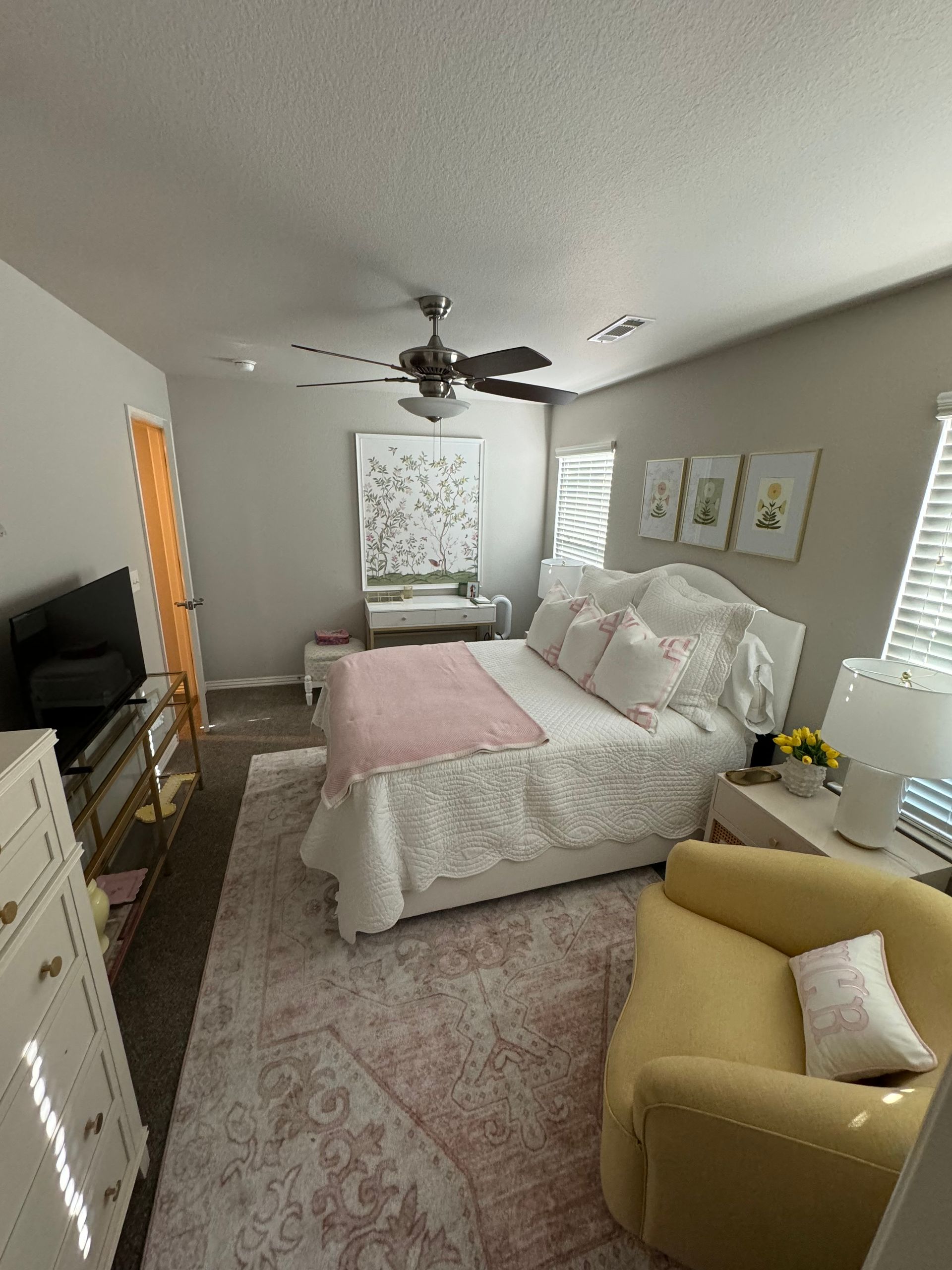 Bedroom with bed, pink accents, yellow chair, artwork, and a TV.