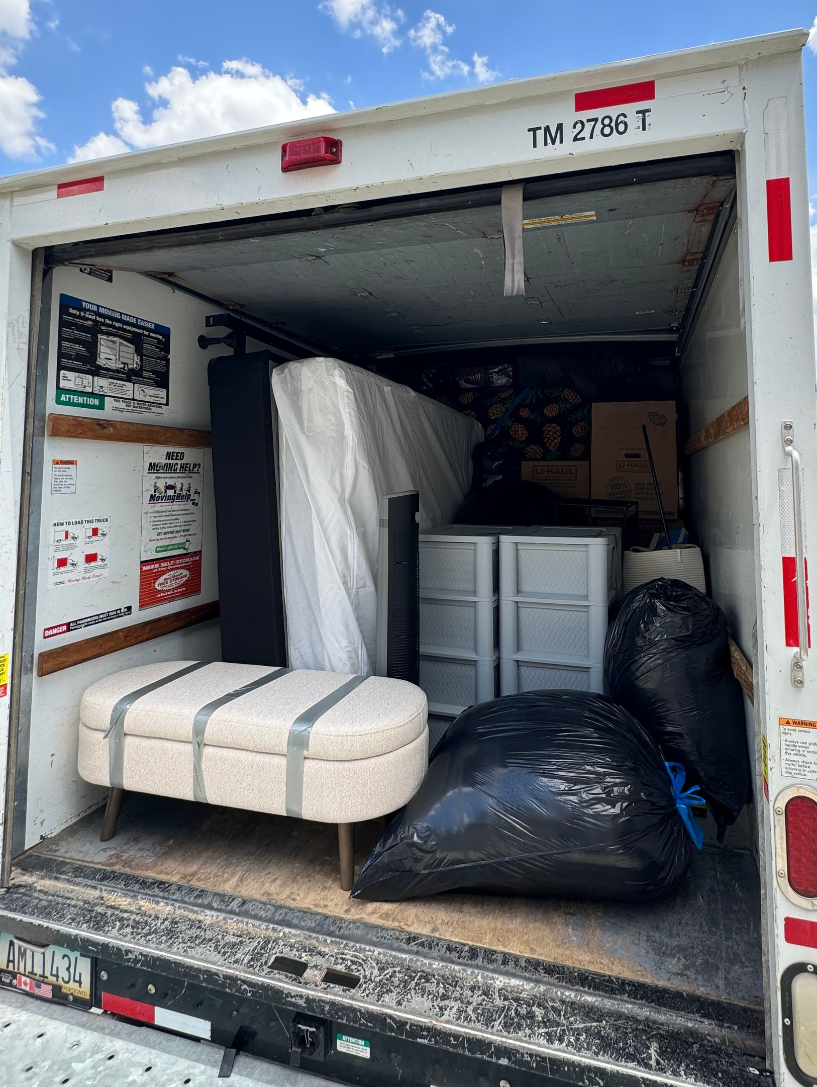 Truck cargo area filled with furniture and boxes; includes a bed, bench, and trash bags.