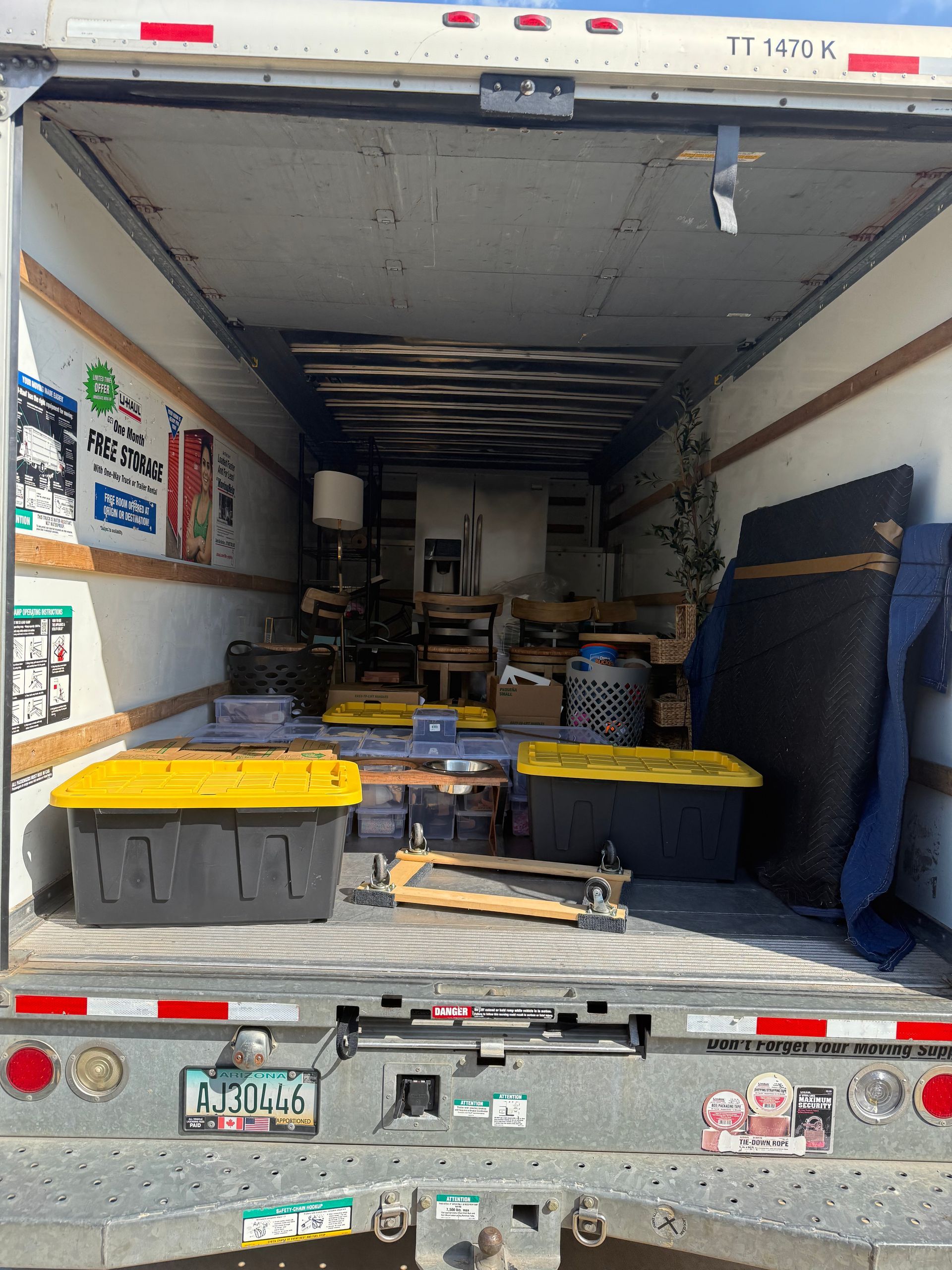 Interior of a moving truck filled with furniture, boxes, and a lamp. The ramp is down, ready for loading.