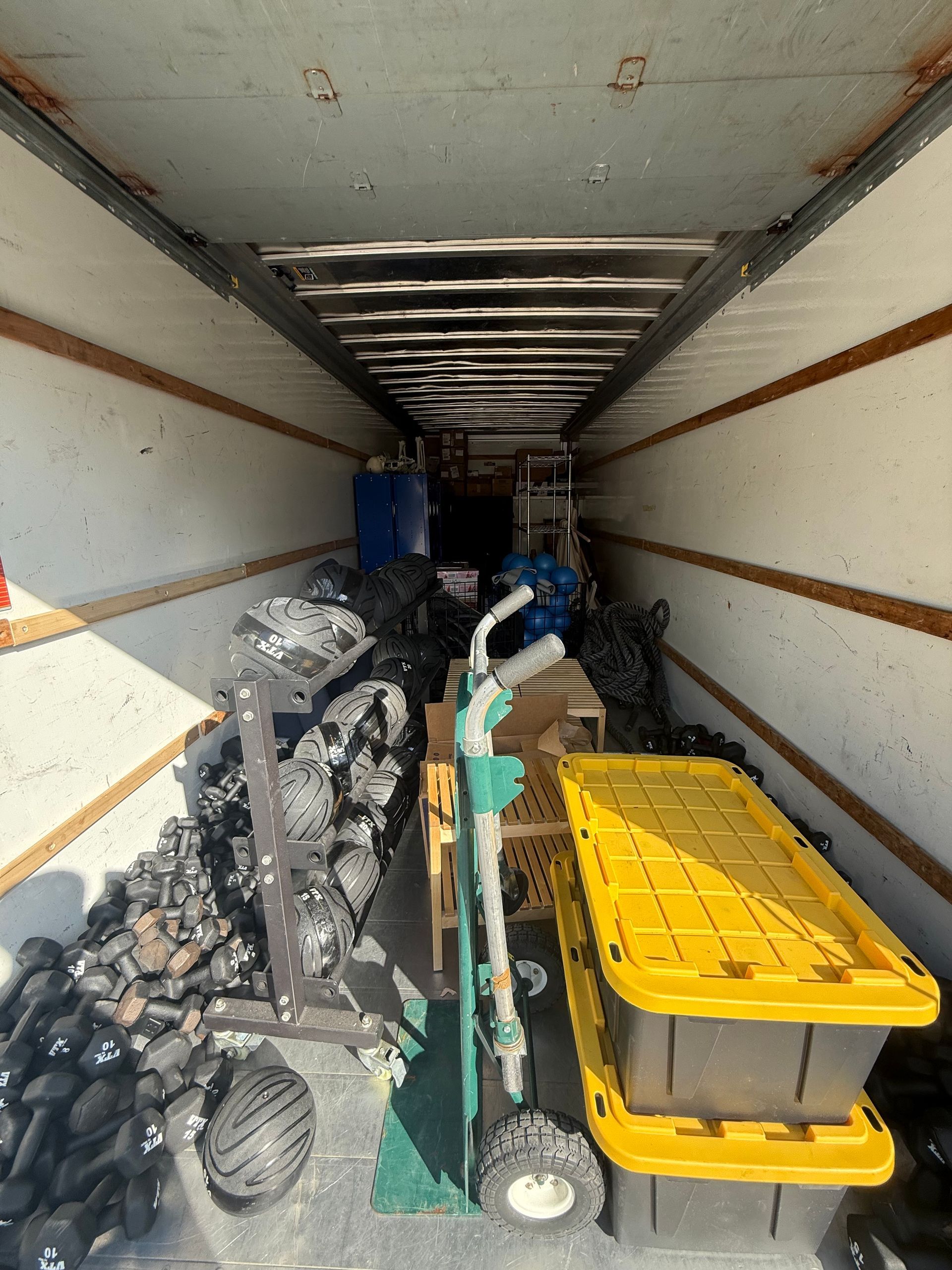 Inside of a moving truck with weights, a hand truck, and storage bins.