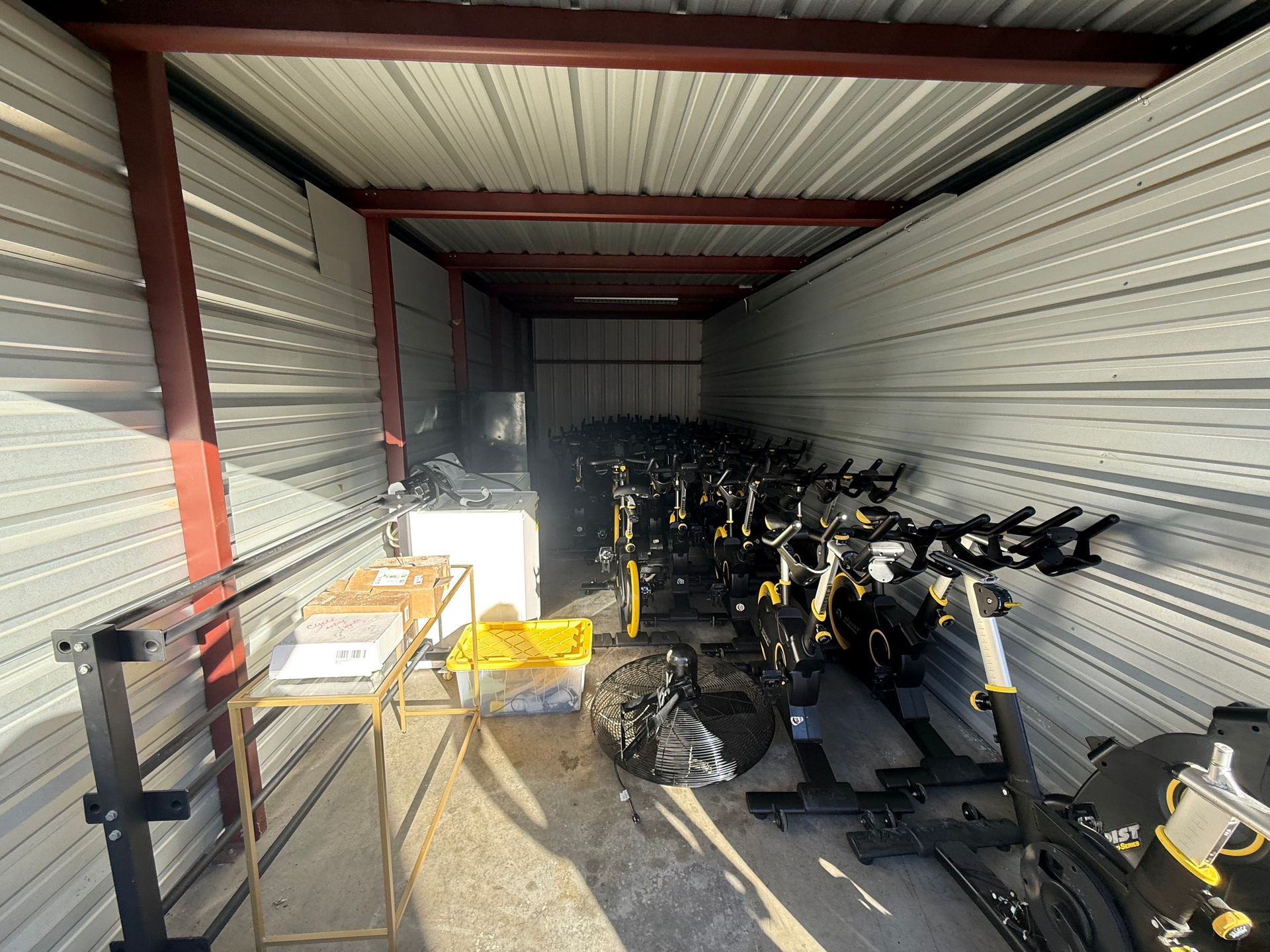 Storage unit packed with stationary exercise bikes. Metal walls, ceiling, and support beams. Yellow and black bikes.