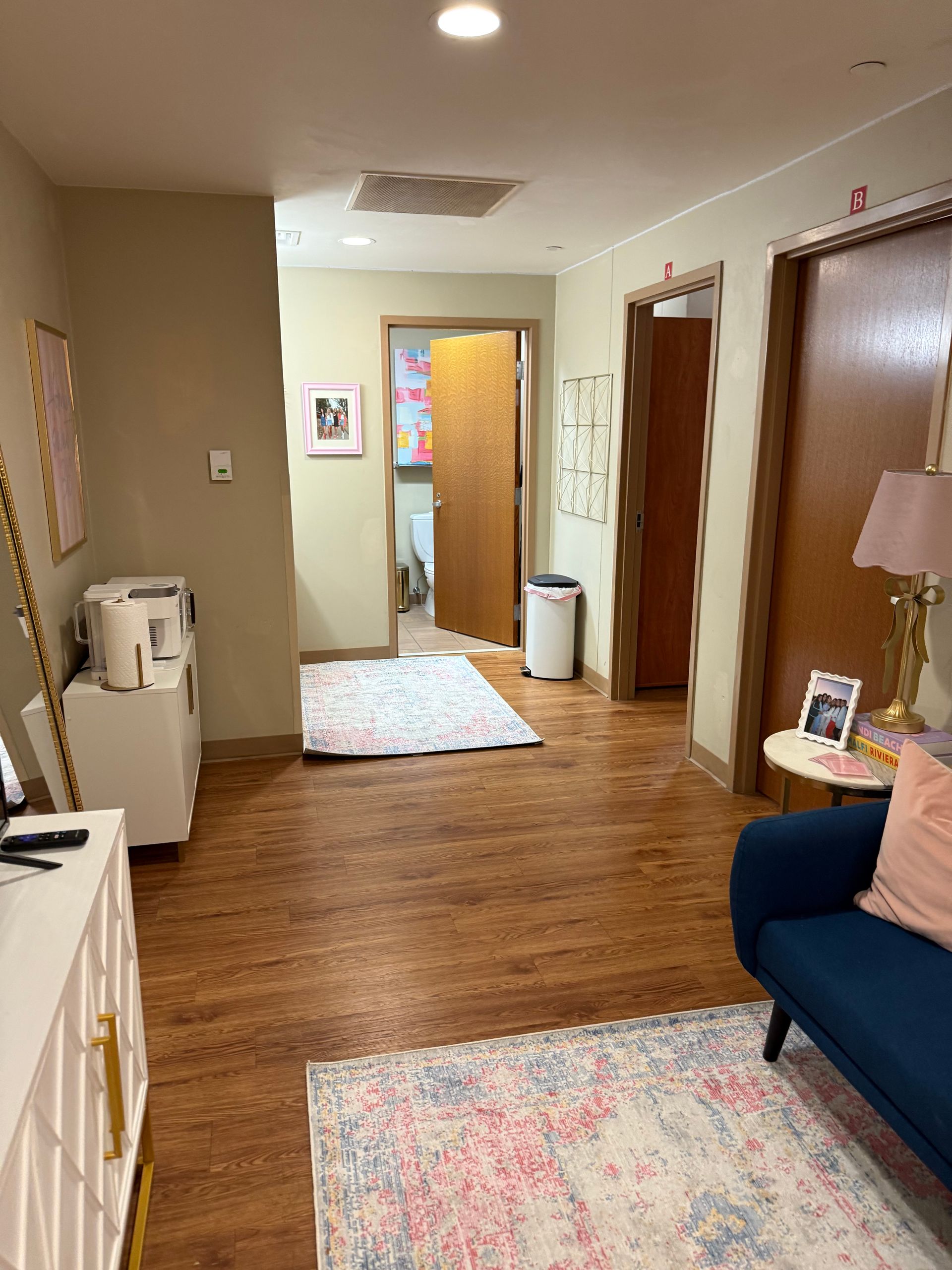 Hallway with wood floors, cream walls, and blue sofa; multiple doorways, and rugs.