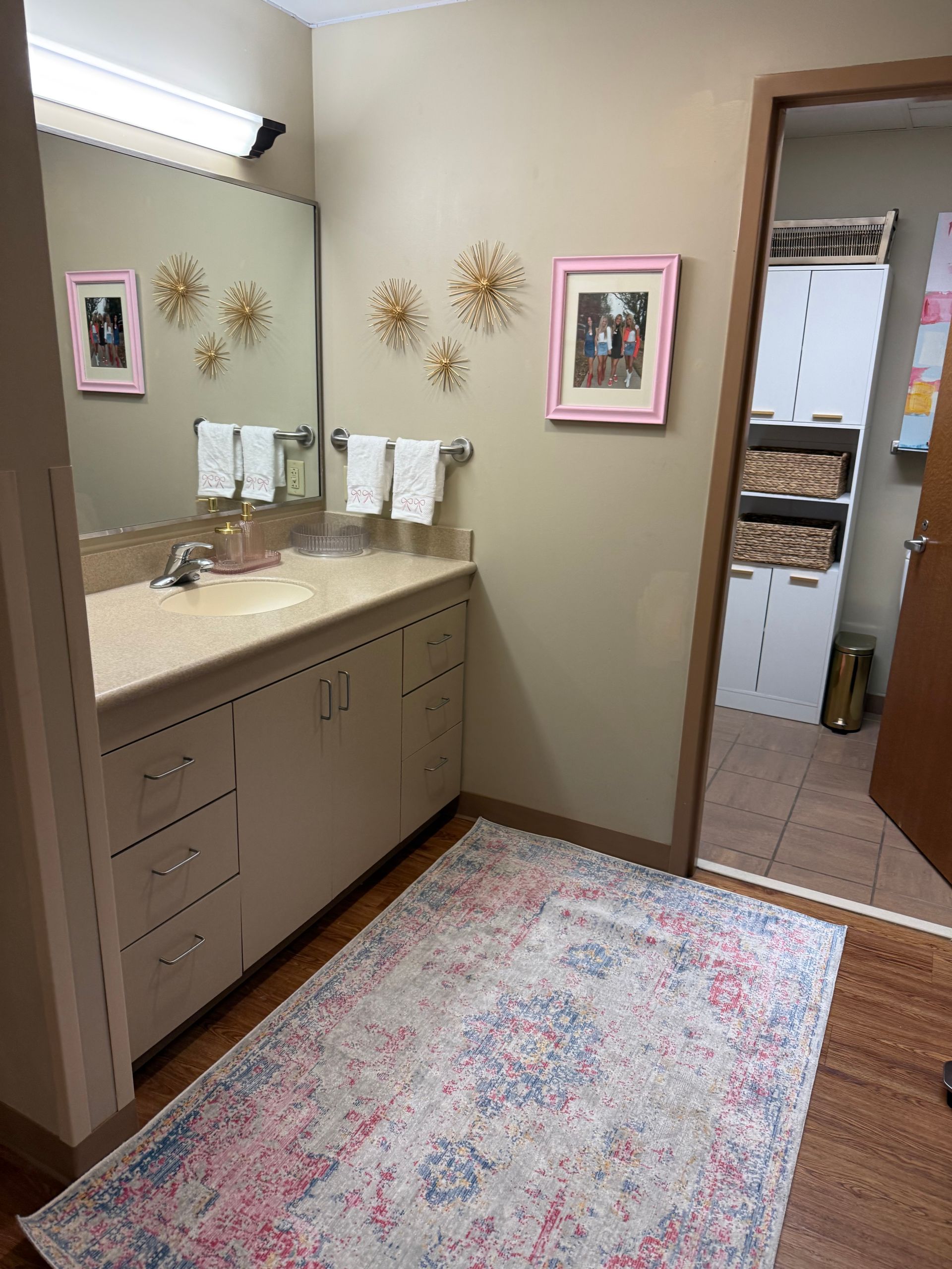 Bathroom with tan walls, vanity, rug, and doorway to storage area. Pink accents.