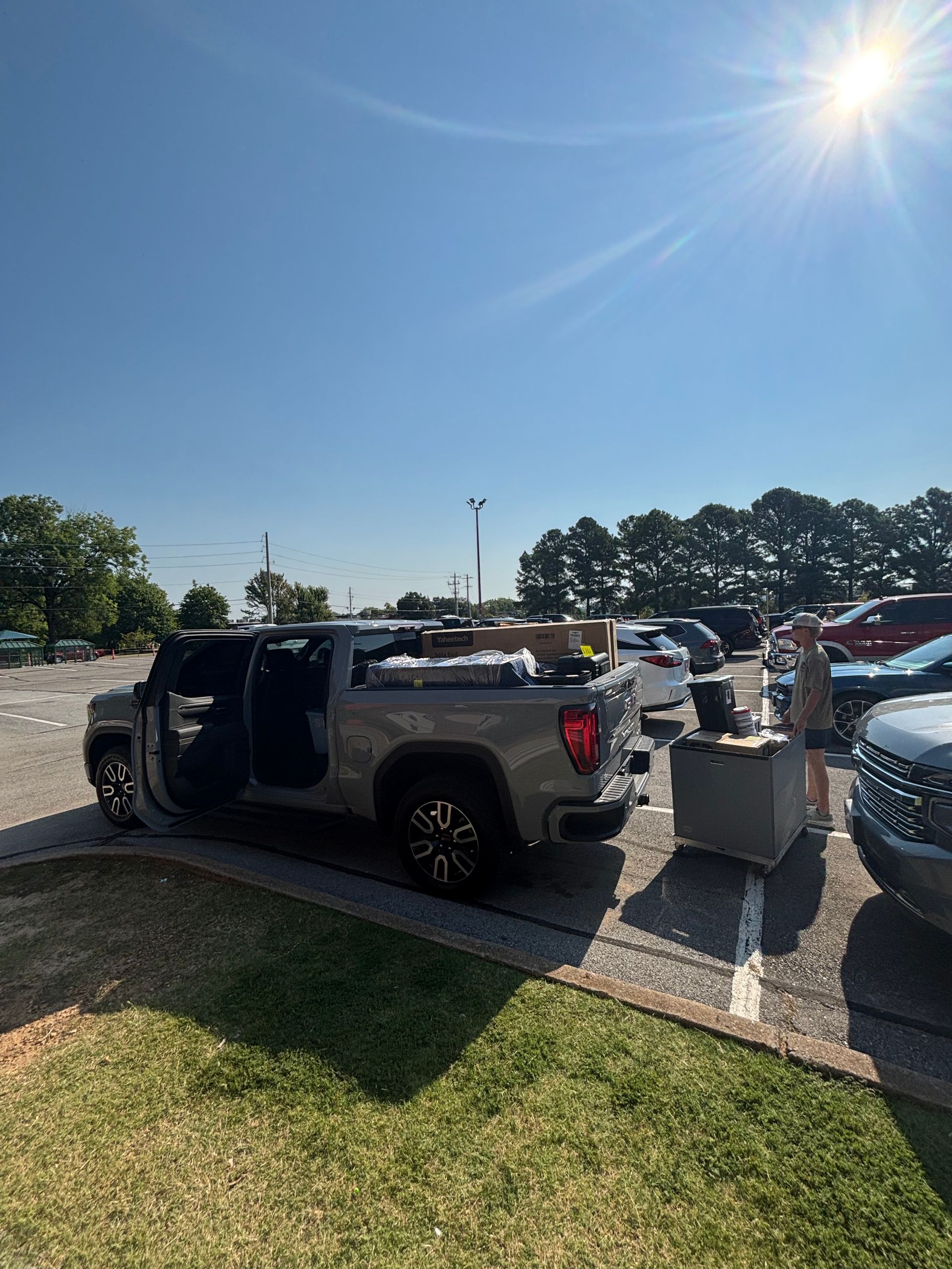 A gray pickup truck with doors open in a parking lot on a sunny day, next to other vehicles.