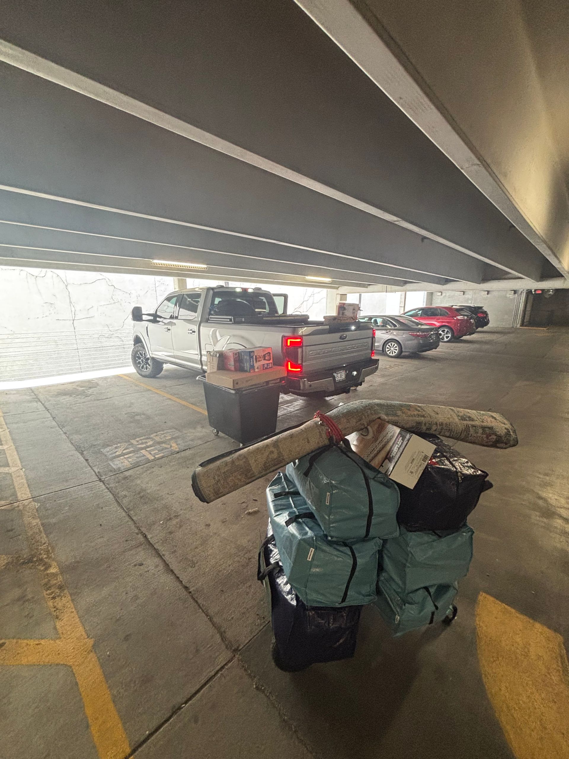 Truck loading with luggage in a parking garage. Teal bags, rug, and boxes are ready to load.