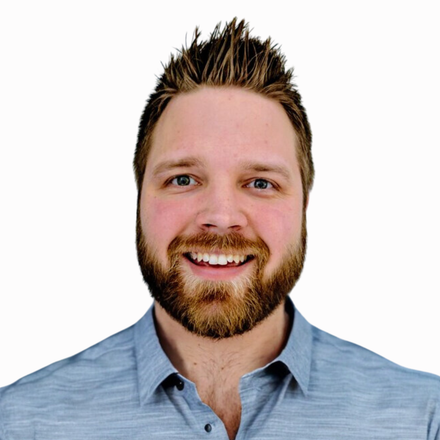 A man with a beard is smiling and wearing a blue shirt