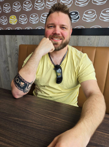 A man with a beard is smiling and wearing a blue shirt