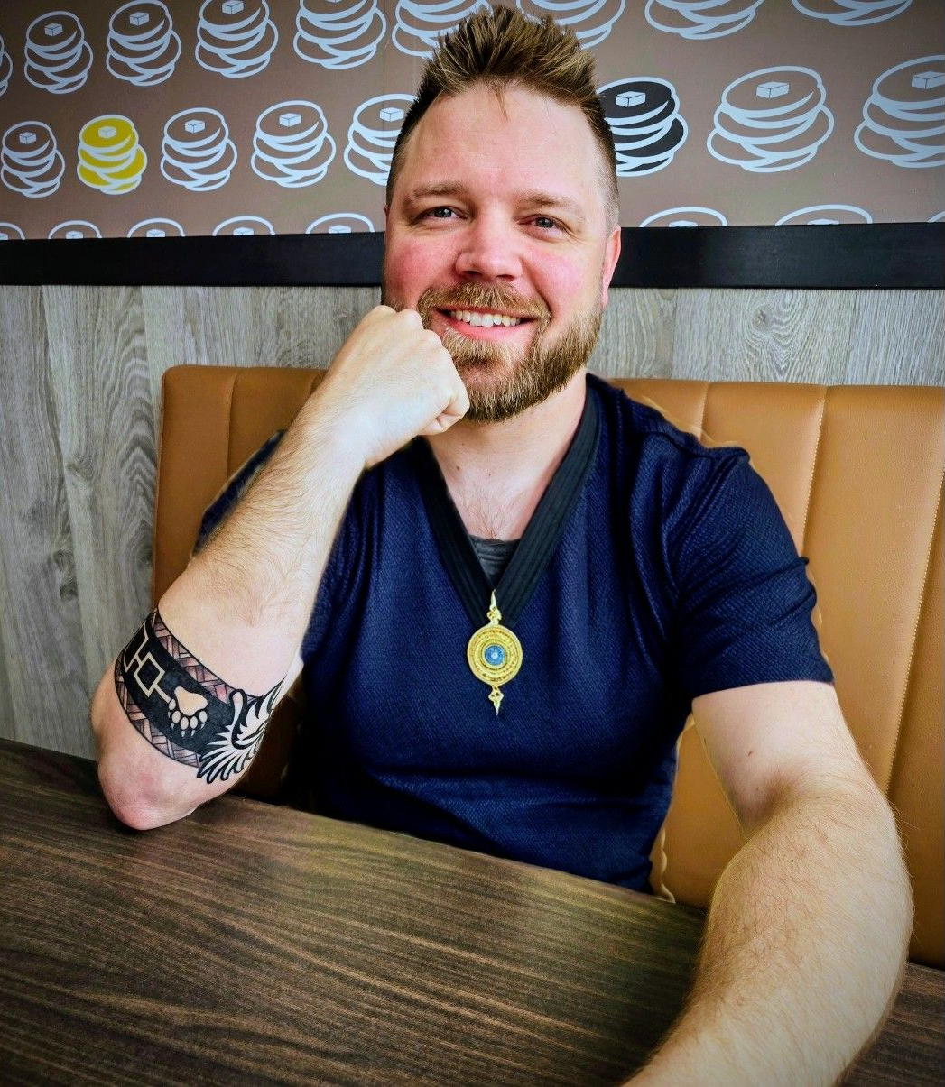 A man with a beard is smiling and wearing a blue shirt