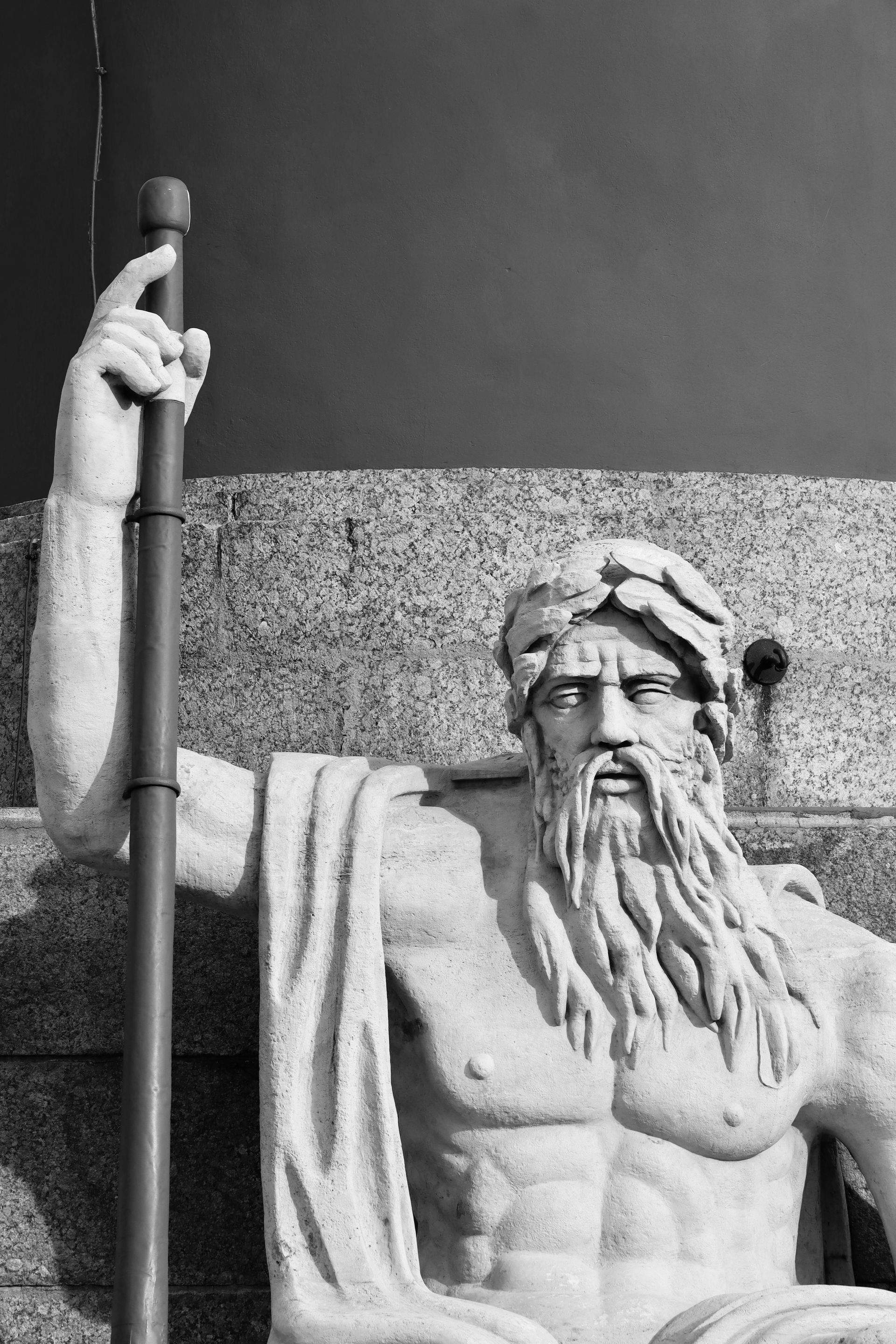 Statue of a bearded man, possibly a god, holding a staff. Black and white.