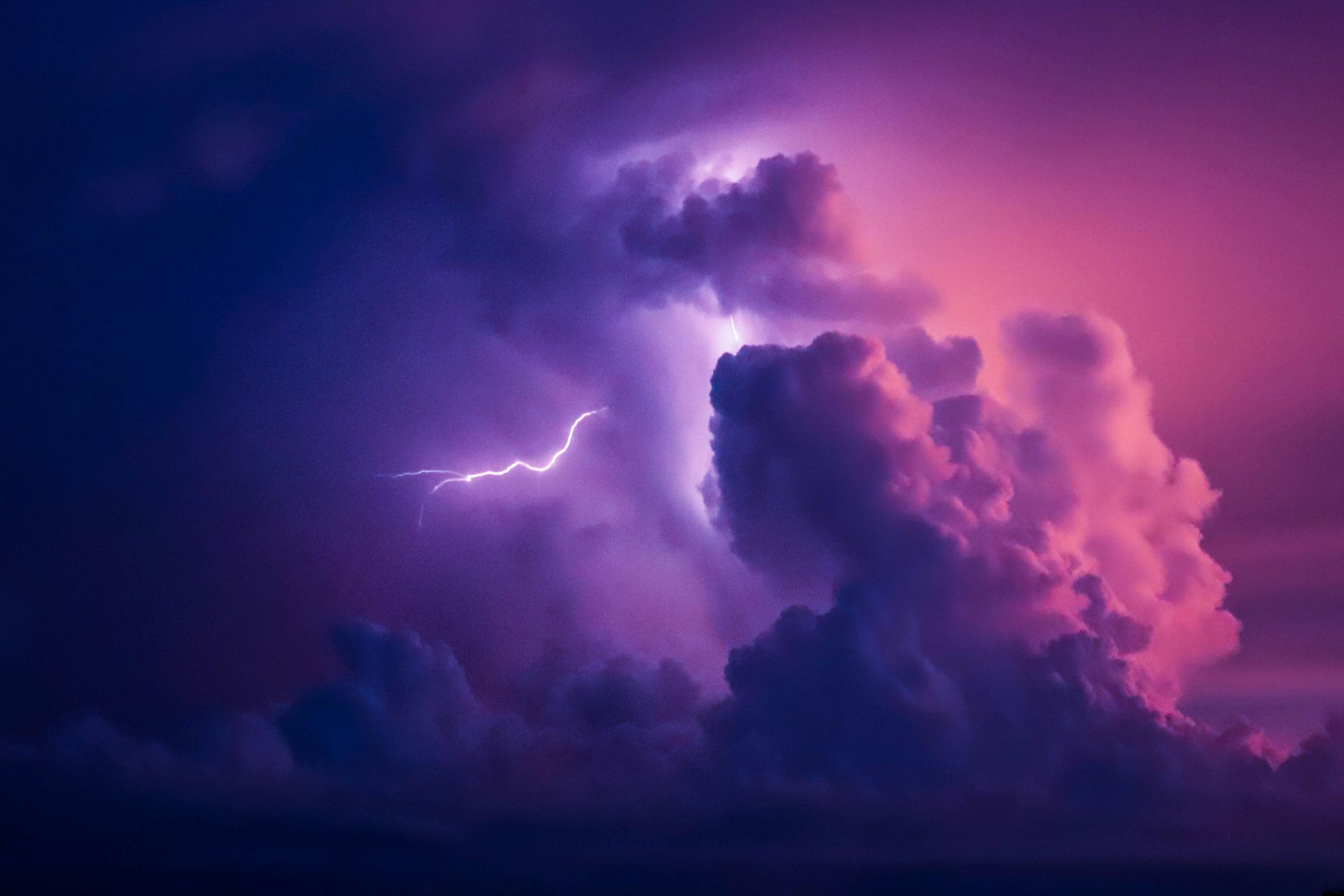 Lightning bolt striking through purple and pink storm clouds.