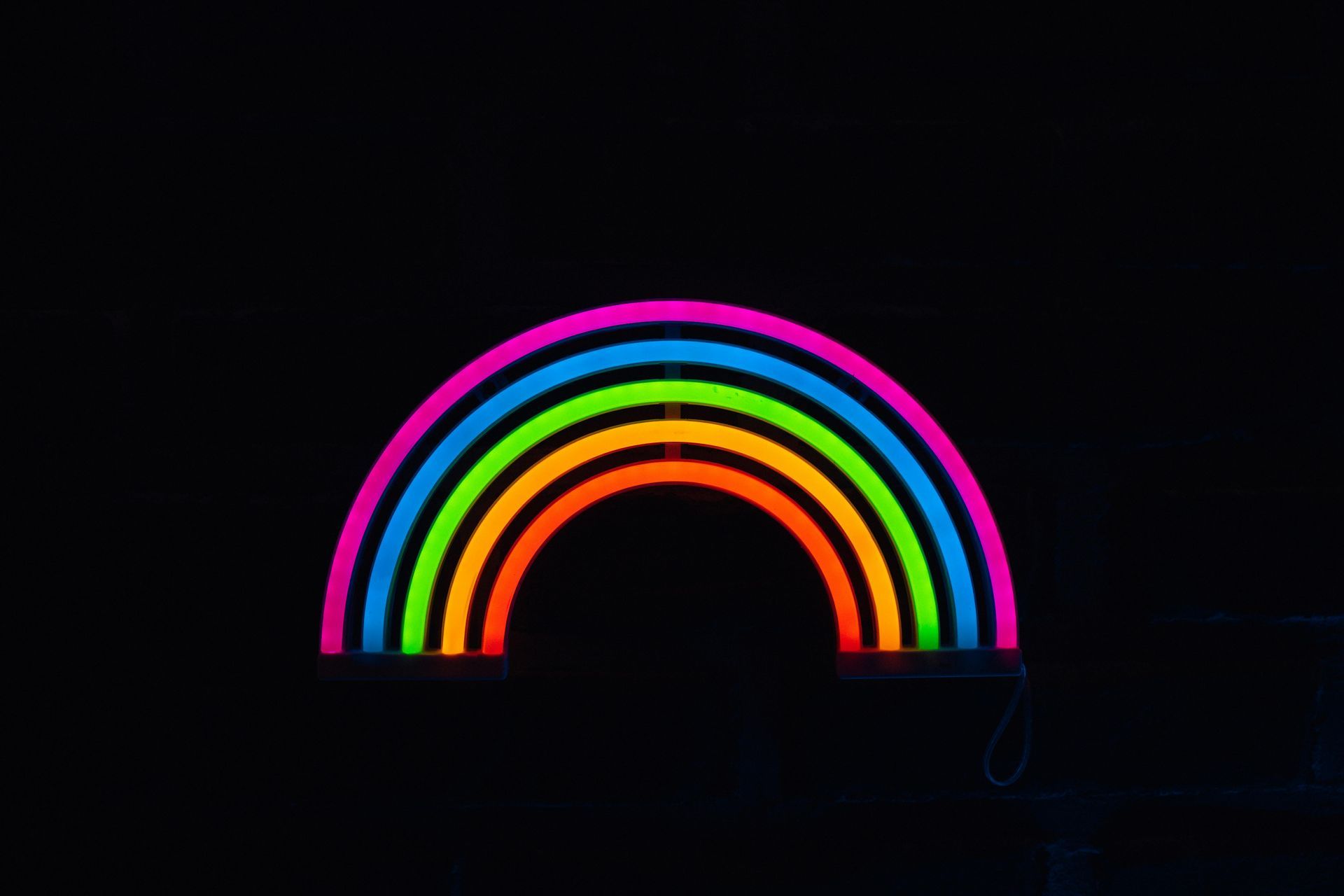 Neon rainbow in pink, blue, green, orange, and yellow arches on a black background.