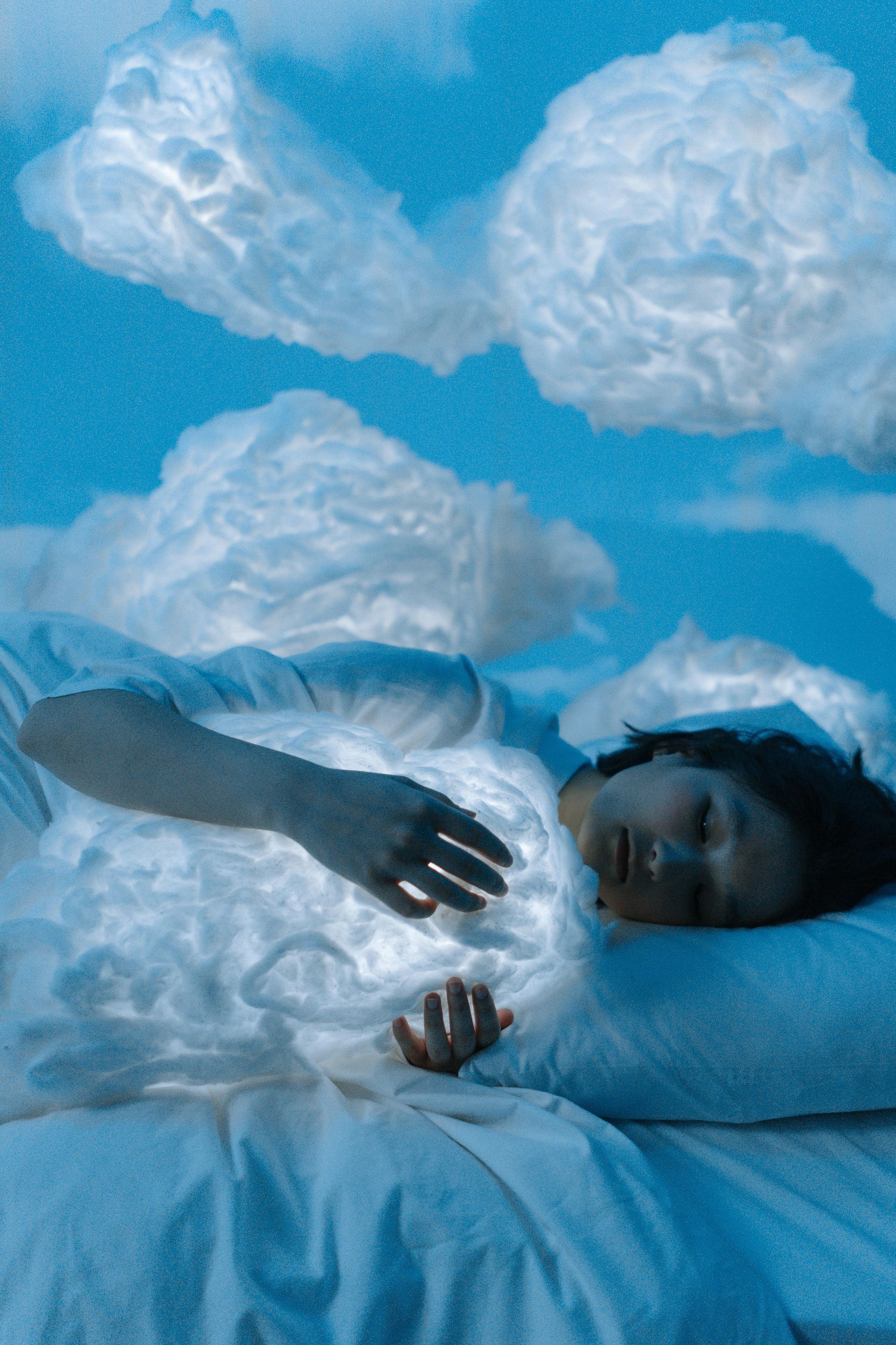 A person lying in bed, surrounded by illuminated cloud-shaped lights against a blue sky.
