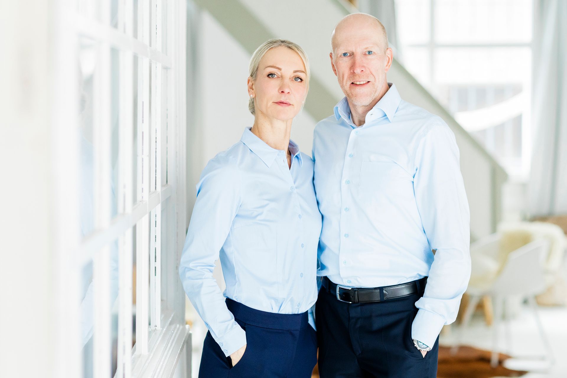 Zwei Personen in identischen hellblauen Hemden mit Knopfleiste stehen nebeneinander in einem hellen, modernen Büroraum.