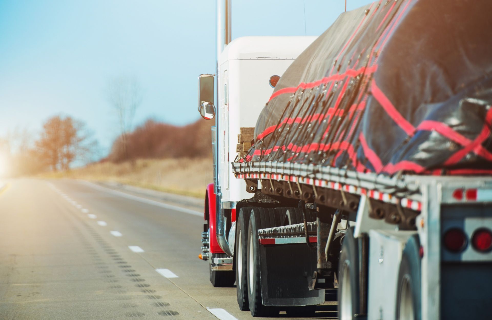 A semi truck with a tarp on the back is driving down a highway.