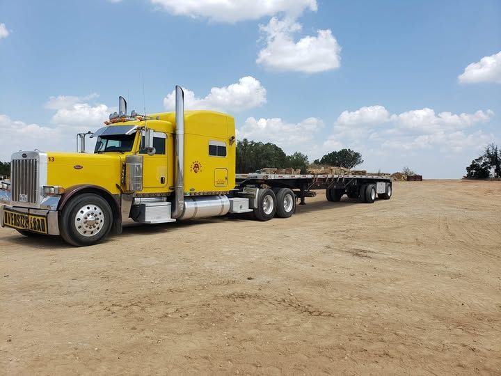 A yellow semi truck is parked in a dirt field.