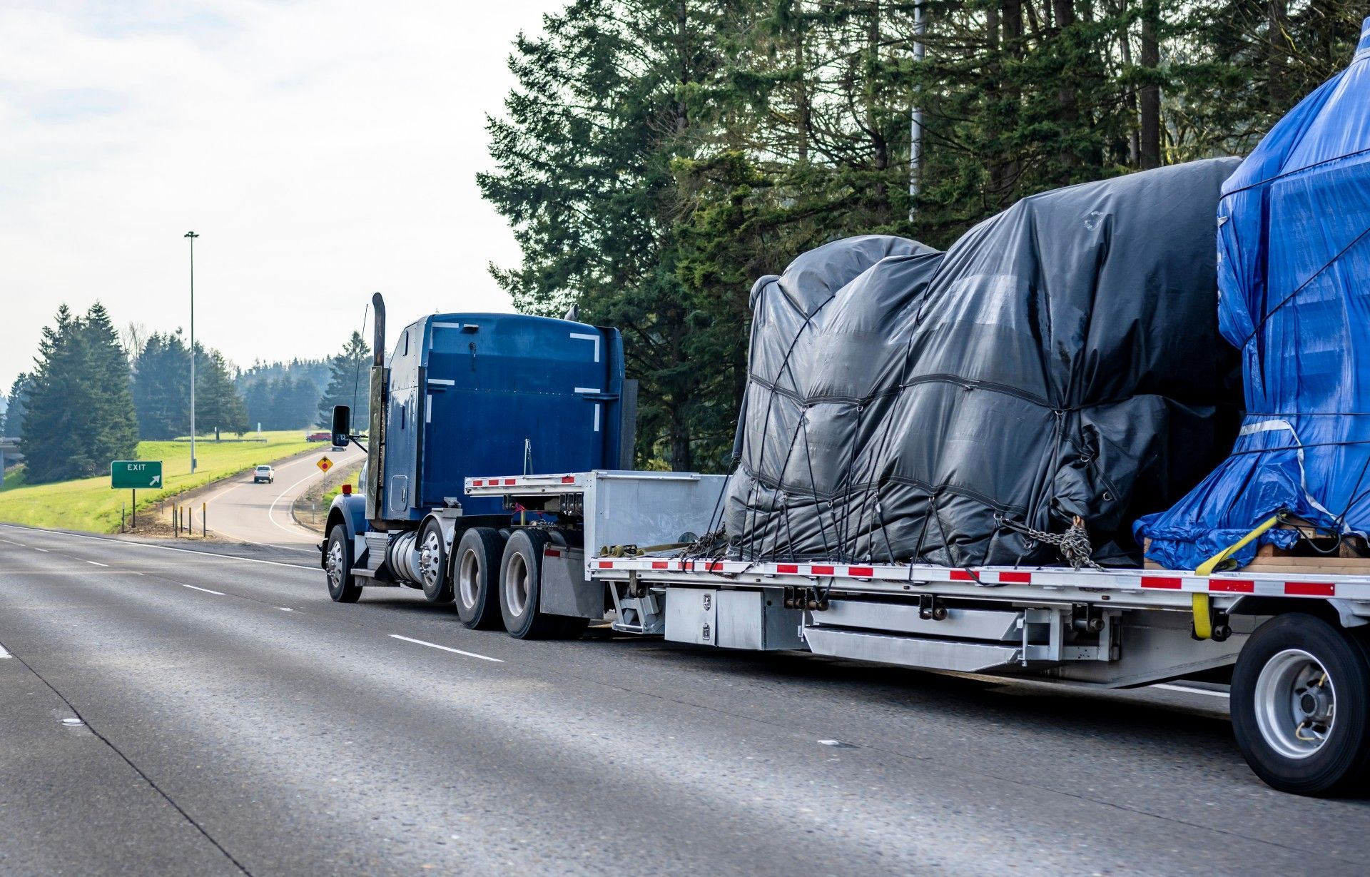 A semi truck is driving down a highway with a trailer carrying a large object.