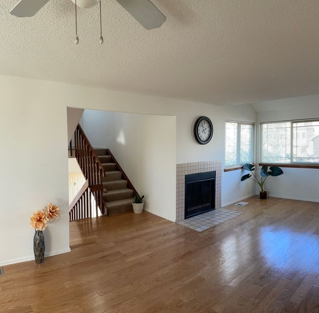 A living room with a fireplace and stairs and a ceiling fan