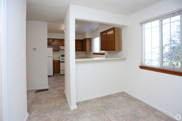 An empty room with a window and a kitchen in the background