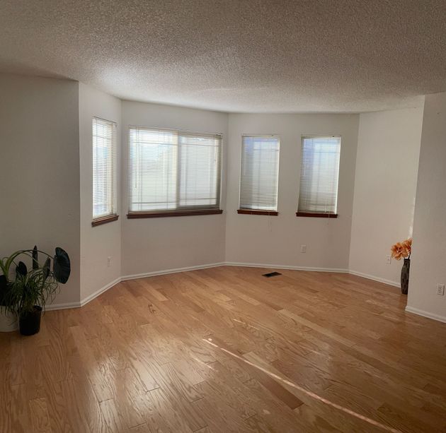 An empty living room with hardwood floors and three windows.