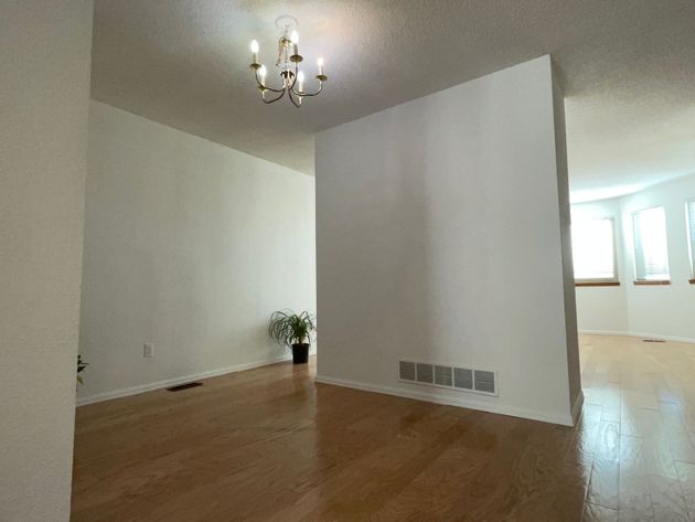 An empty room with hardwood floors and a chandelier hanging from the ceiling.