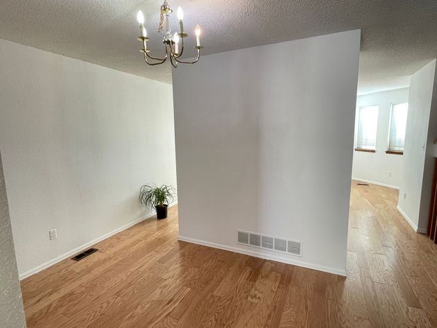 An empty dining room with hardwood floors and a chandelier hanging from the ceiling.