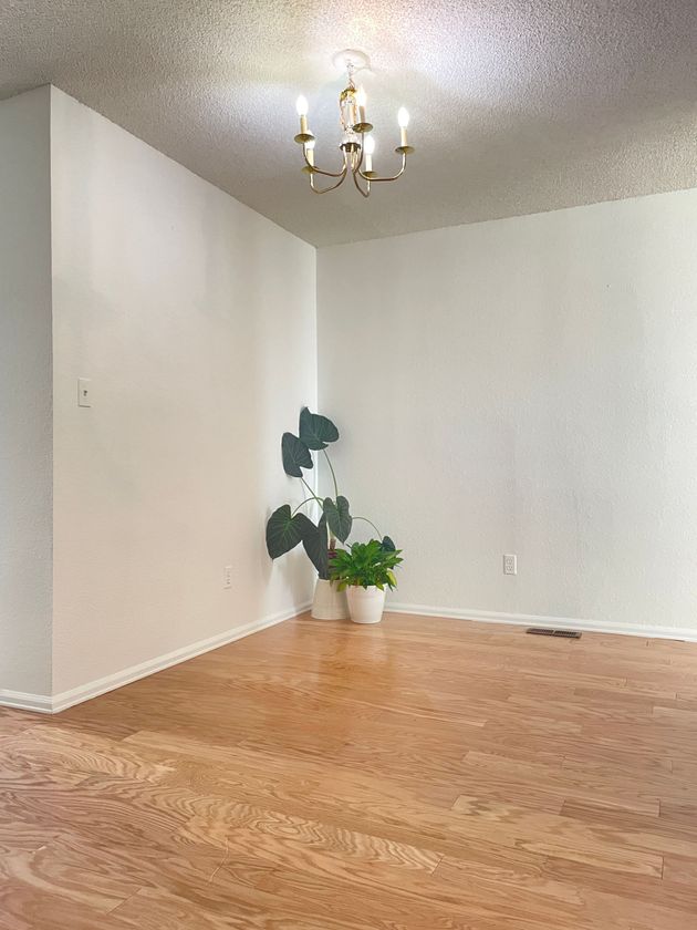 An empty living room with hardwood floors and a chandelier hanging from the ceiling.