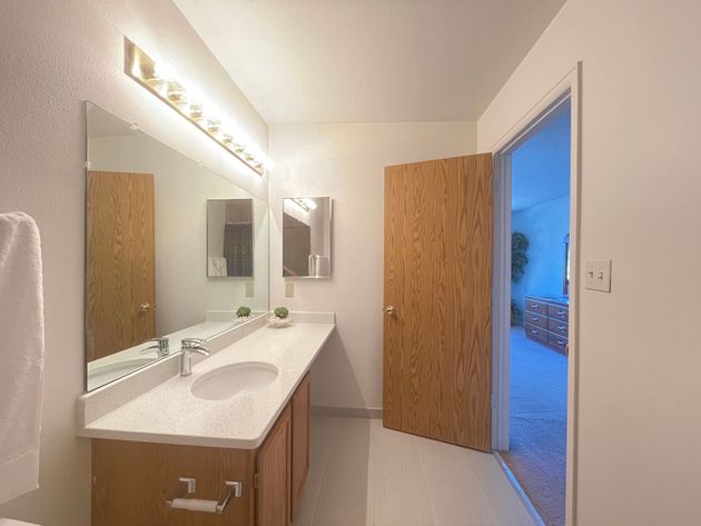 A bathroom with two sinks , a mirror and a door leading to a bedroom.