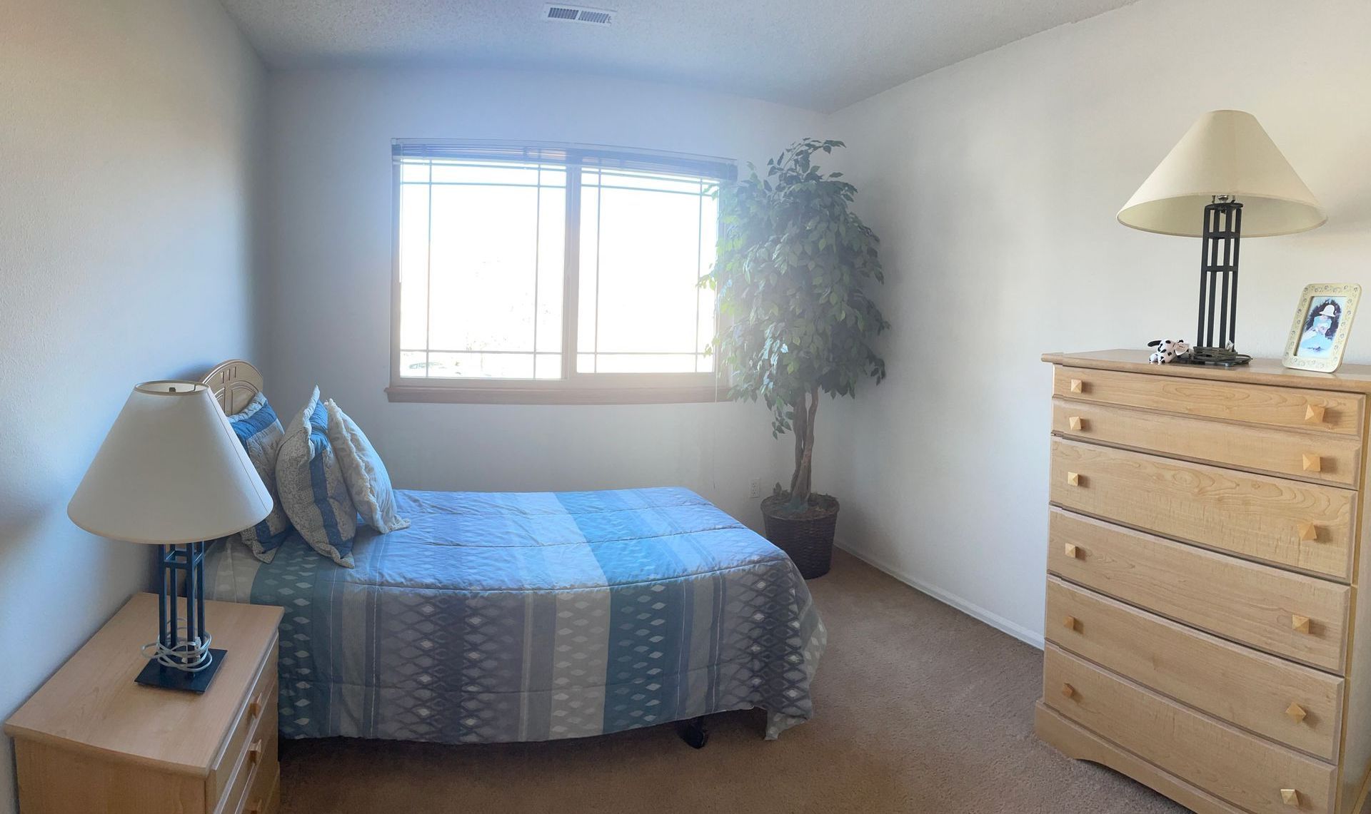 A bedroom with a bed , dresser , nightstand , lamp and window.