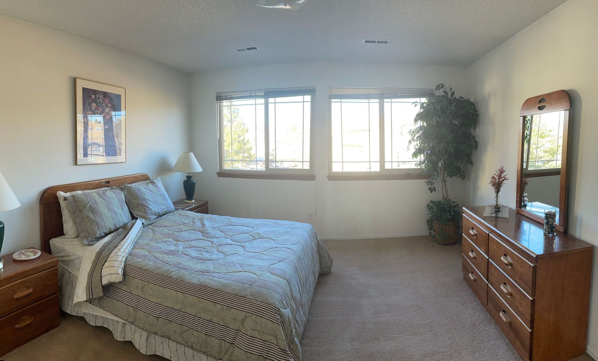 A bedroom with a bed , dresser , mirror and window.