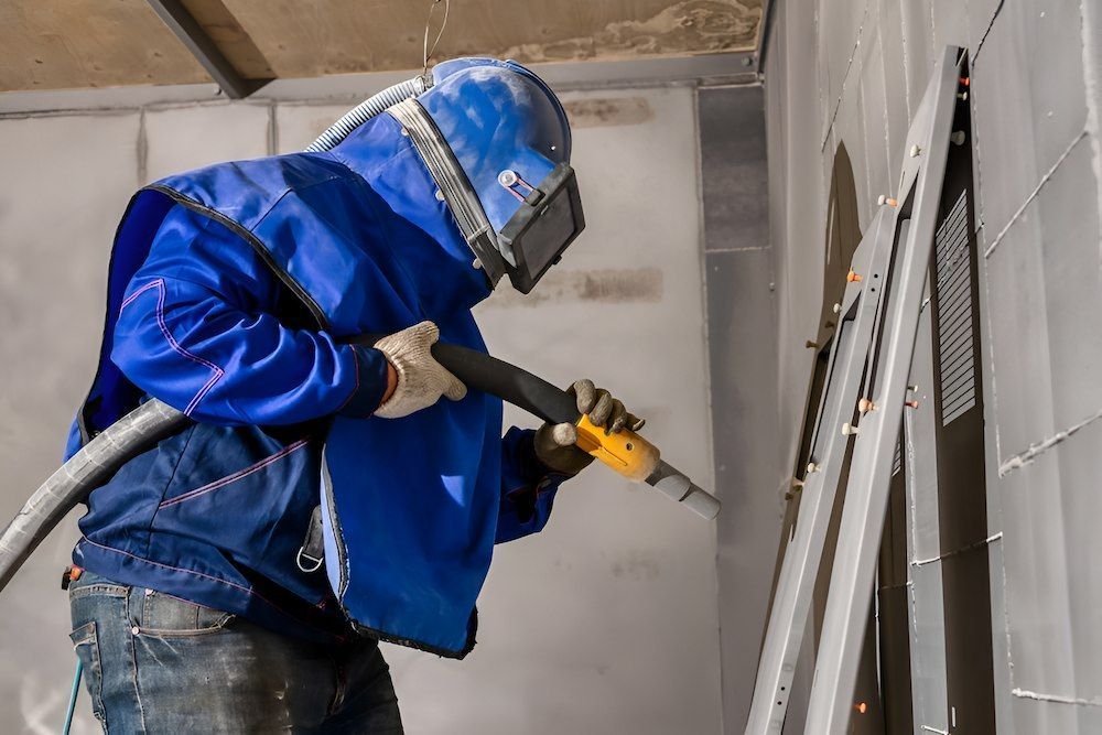 A Man Is Sandblasting A Wall With A Machine — ADK Coatings In Tannum Sands, QLD