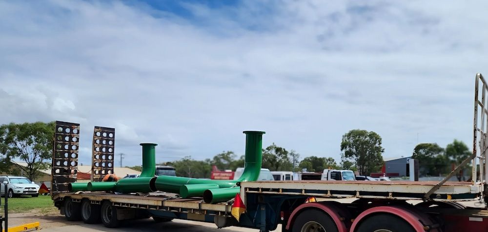 A Truck Is Carrying Green Pipes On A Flatbed Trailer — ADK Coatings In Tannum Sands, QLD
