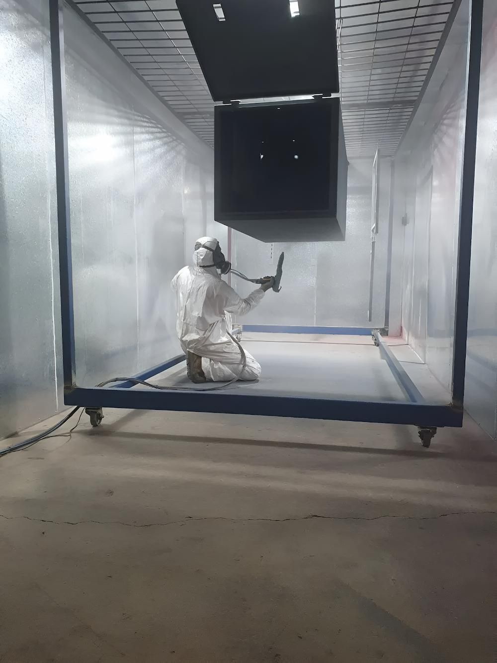 A Man Is Spray Painting A Piece Of Metal In A Room — ADK Coatings In Gladstone, QLD