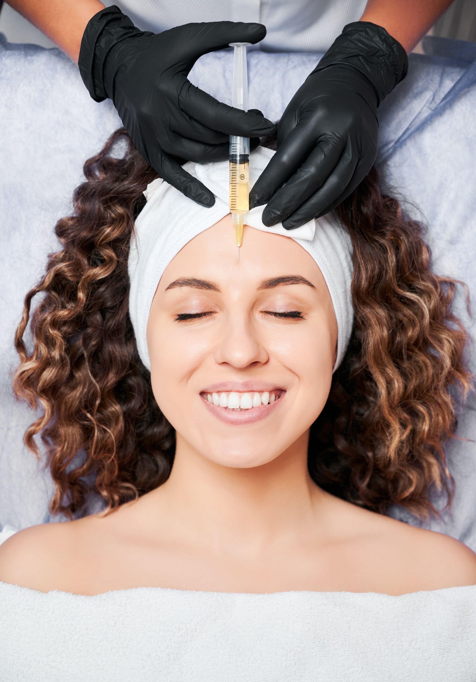 a woman is smiling while getting an injection in her forehead