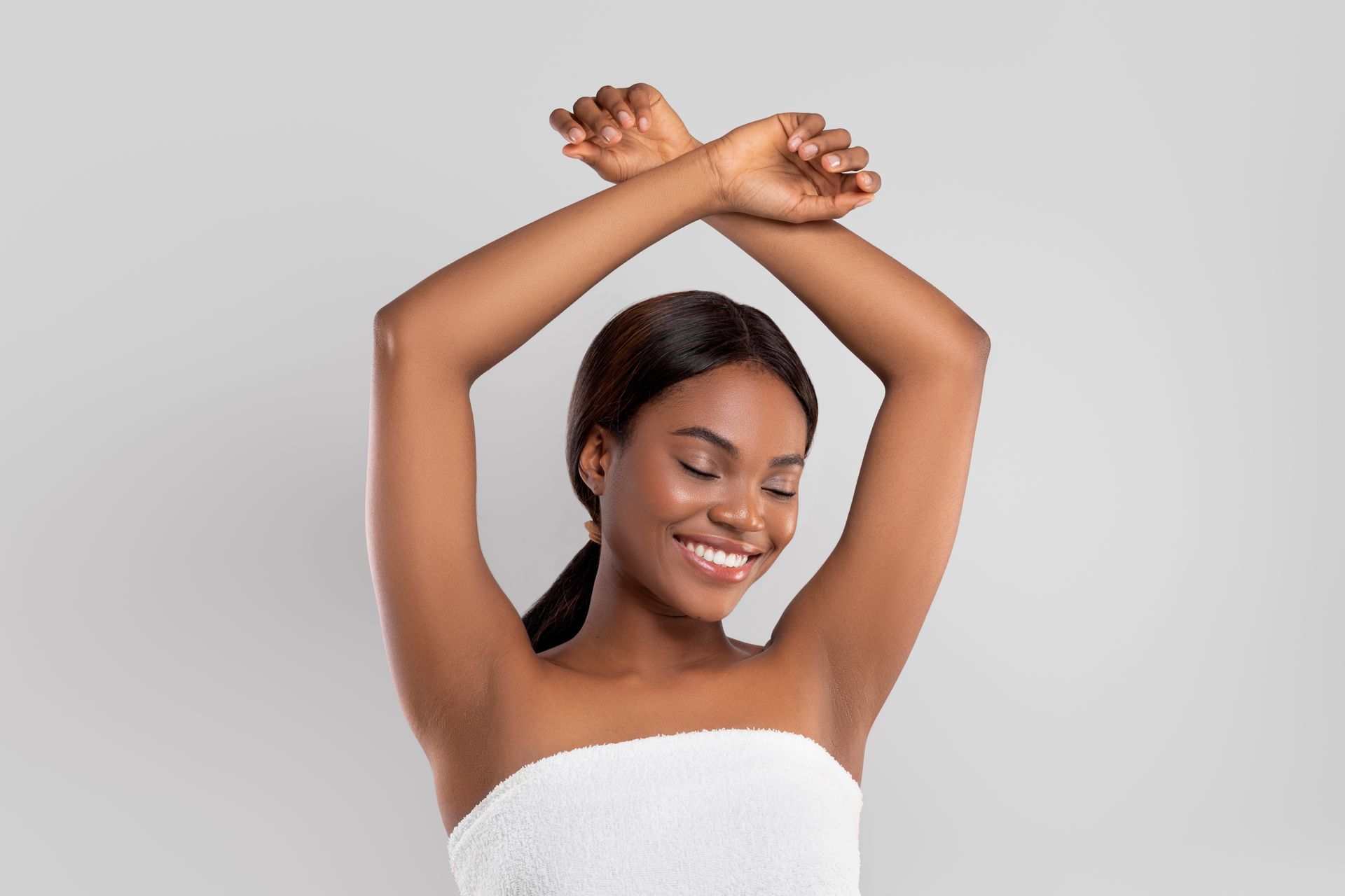 a woman wrapped in a white towel is smiling with her arms in the air .