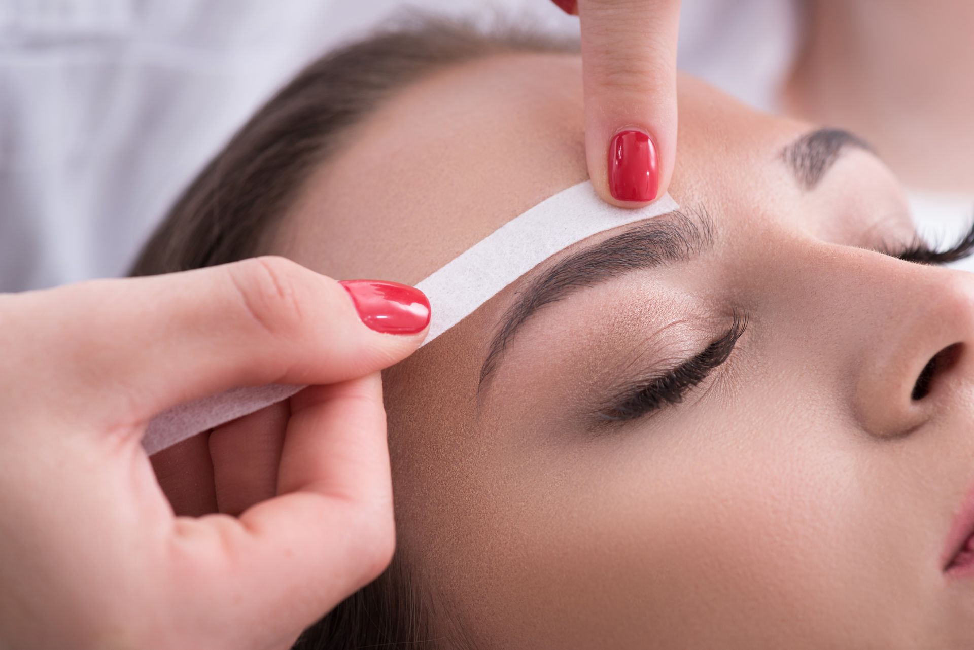 a woman with red nails is getting her eyebrows waxed