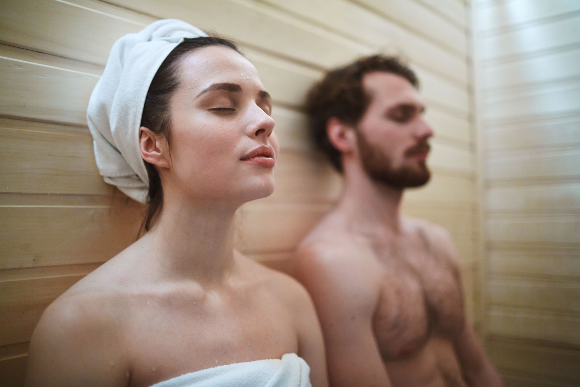 a man and a woman are sitting in a sauna with their eyes closed