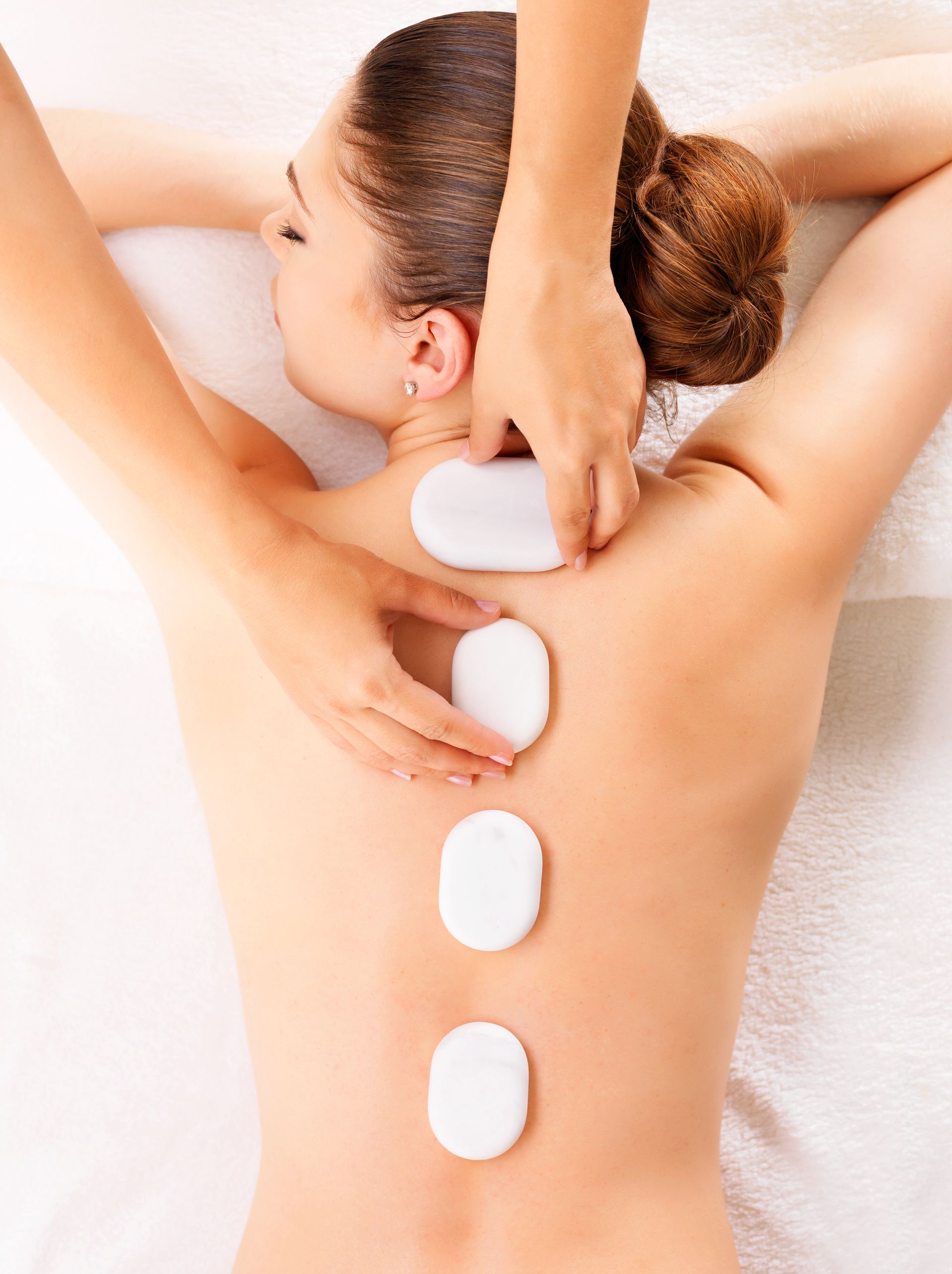 a woman is getting a massage with three white stones on her back