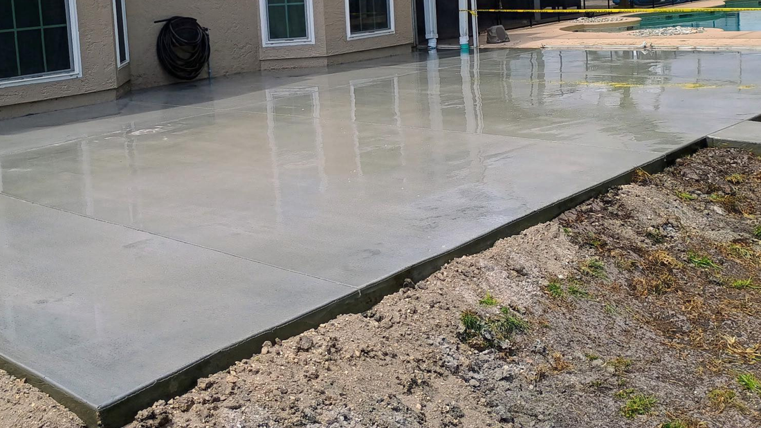 Freshly poured concrete patio next to a beige house, reflecting the sky.