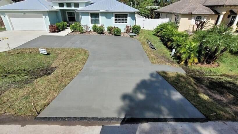 Newly poured concrete driveway in front of a blue house with landscaping.