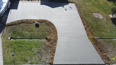 Aerial view of a gray concrete driveway and walkway bordered by grass and mulch.