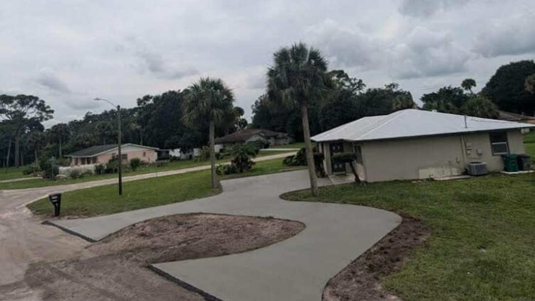 A winding concrete driveway in a suburban neighborhood with trees and overcast skies.