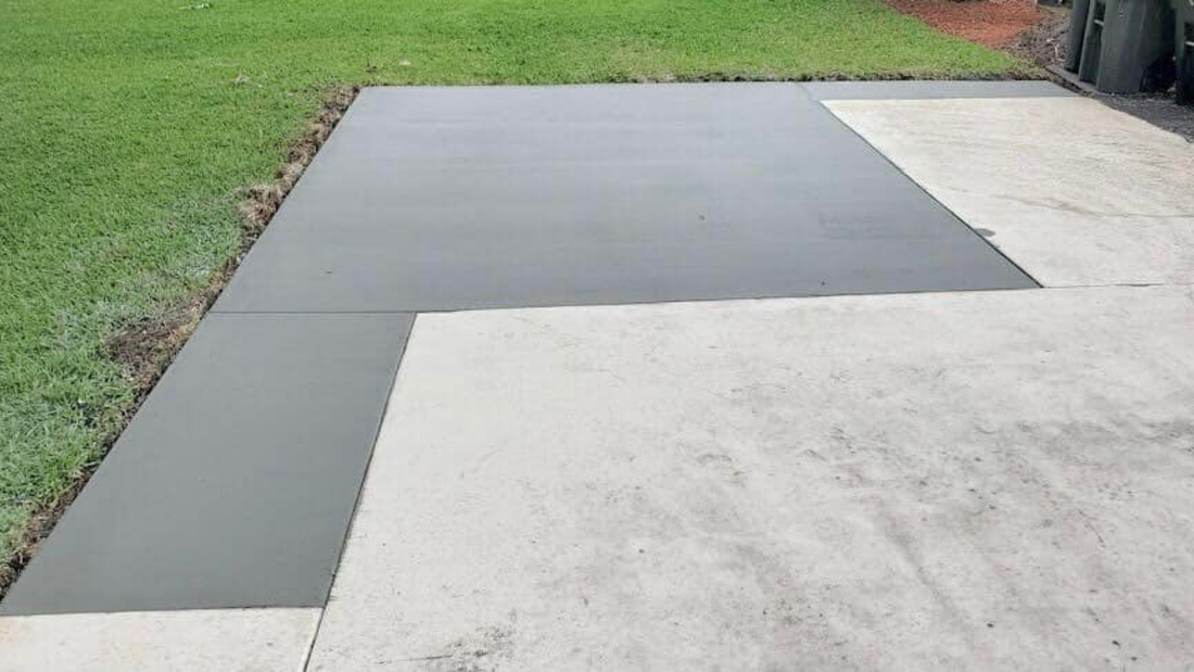 Freshly poured gray concrete next to an older, lighter concrete patio with grass in the background.