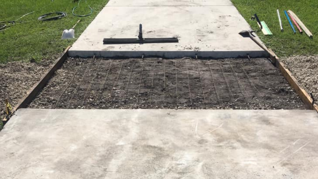 Sidewalk repair in progress: Concrete forms, rebar grid laid, and tools on grass.