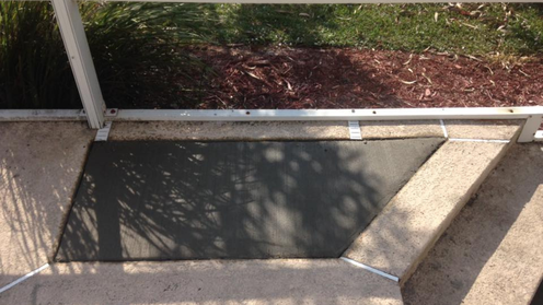 Black mat on concrete floor, under metal railing. Dark mulch and grass in background.