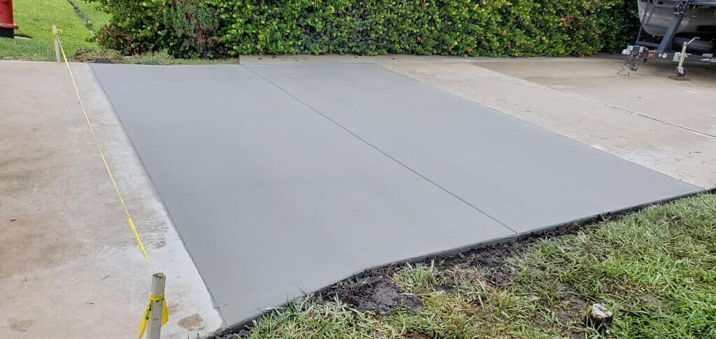 Newly poured concrete driveway with fresh gray surface, alongside existing concrete and grass.