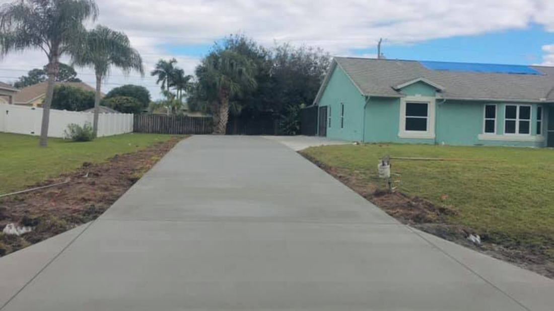 Newly poured concrete driveway leading to a light blue house. Green lawn surrounds it.