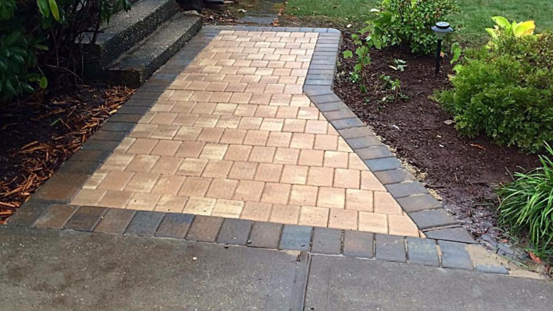 Brick pathway leading to steps, bordered by darker bricks and landscaping.
